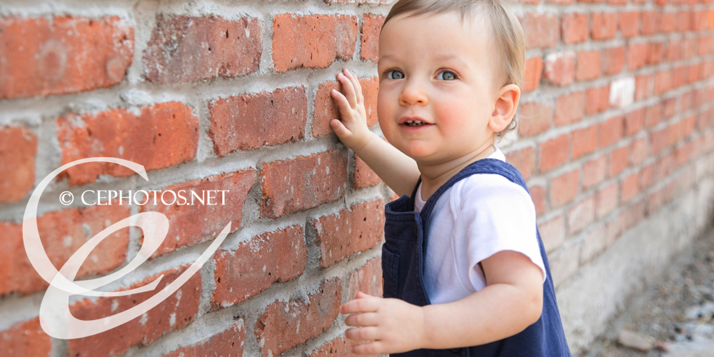 baby boy on red brick wall in overalls denver photographer